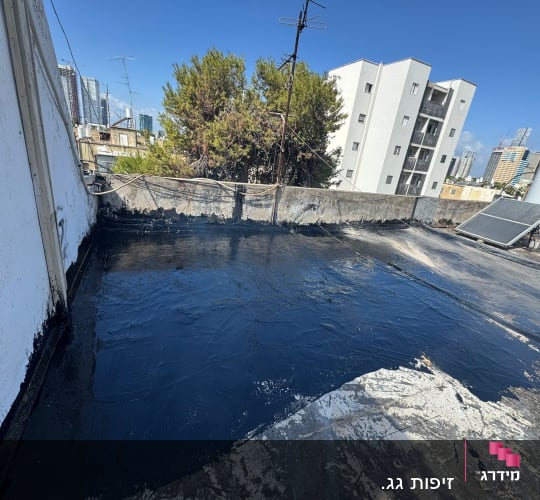 איטום גג עם חומר שחור על רקע בניינים
